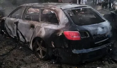 Spalony, stojący na błocie samochód osobowy typu kombi po pożarze, z dymiącym wnętrzem i uszkodzoną karoserią.